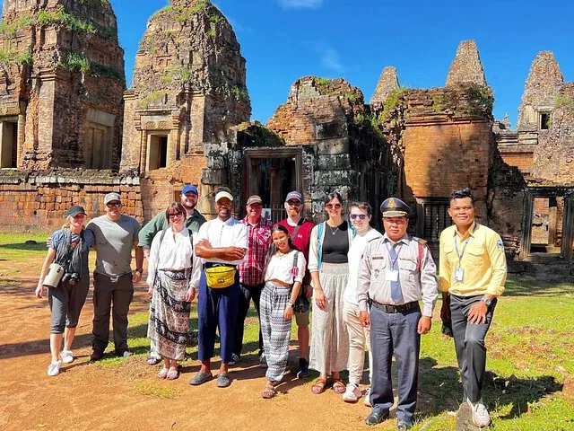 groupe de touristes posant devant des ruines anciennes de temple en pierre